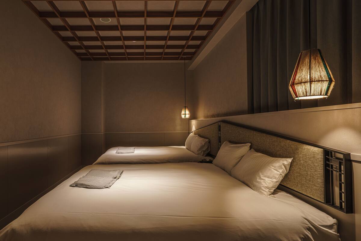 A hotel room with a large bed, a bedside table, a wall-mounted lamp, and a window with curtains.