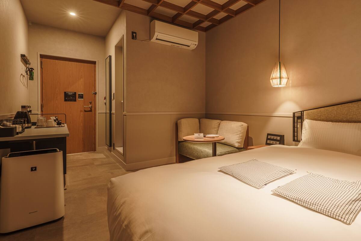 A hotel room with a bed, bedside table, chair, and a desk with a mirror.