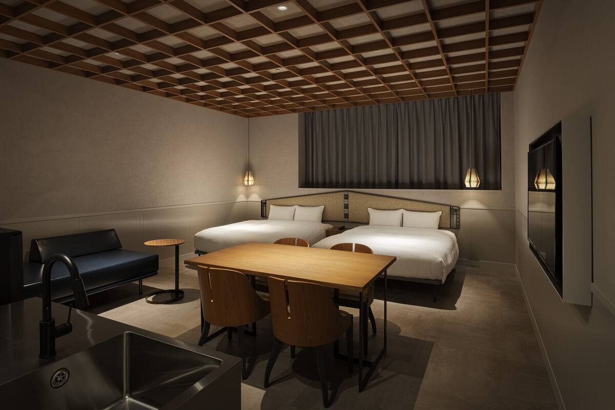 A modern hotel room with a wooden ceiling, a sofa, a dining table with chairs, two beds, and a large window with curtains.