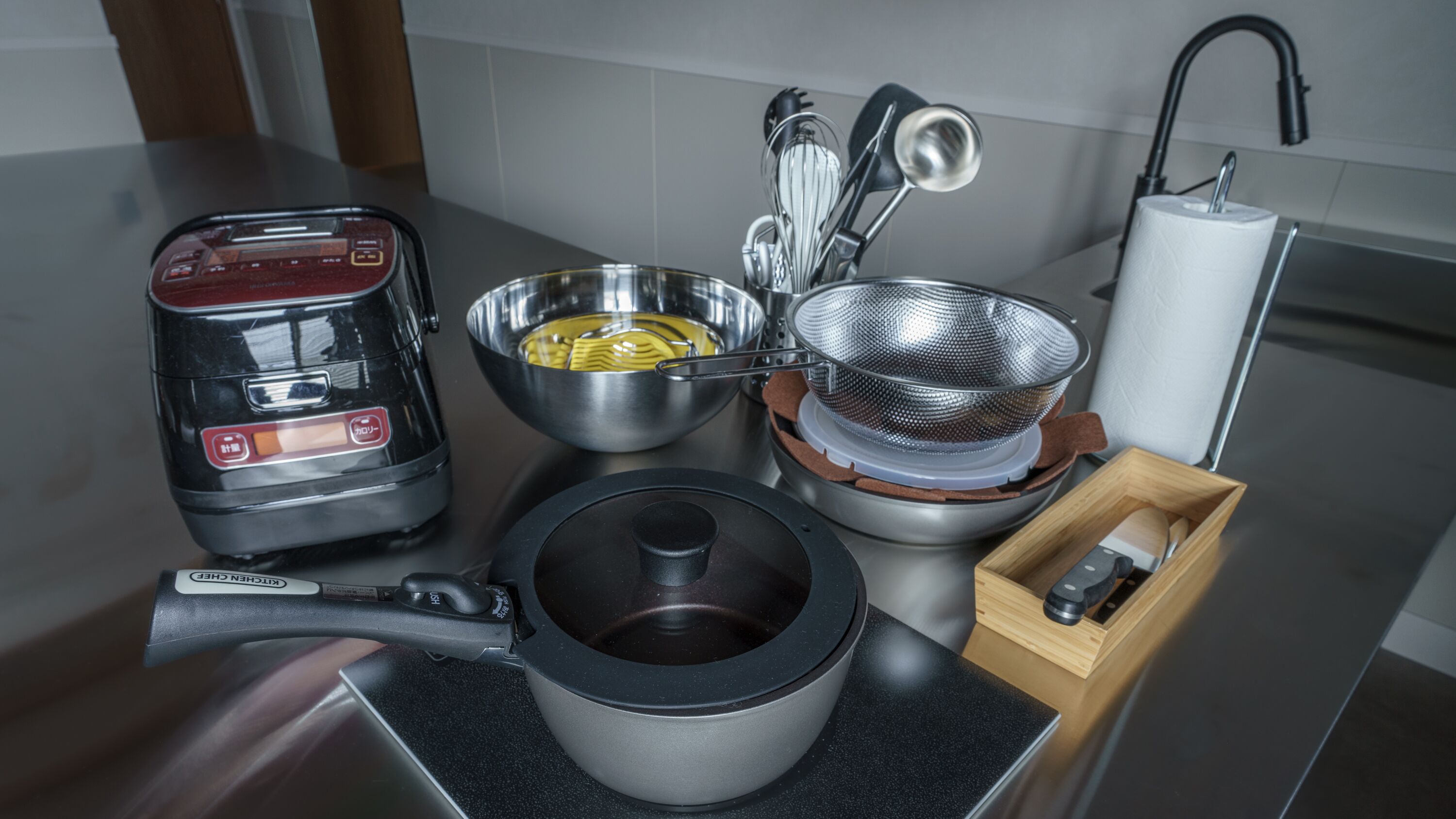 Un plan de travail de cuisine avec une machine à café, une casserole, une passoire et une boîte en bois.