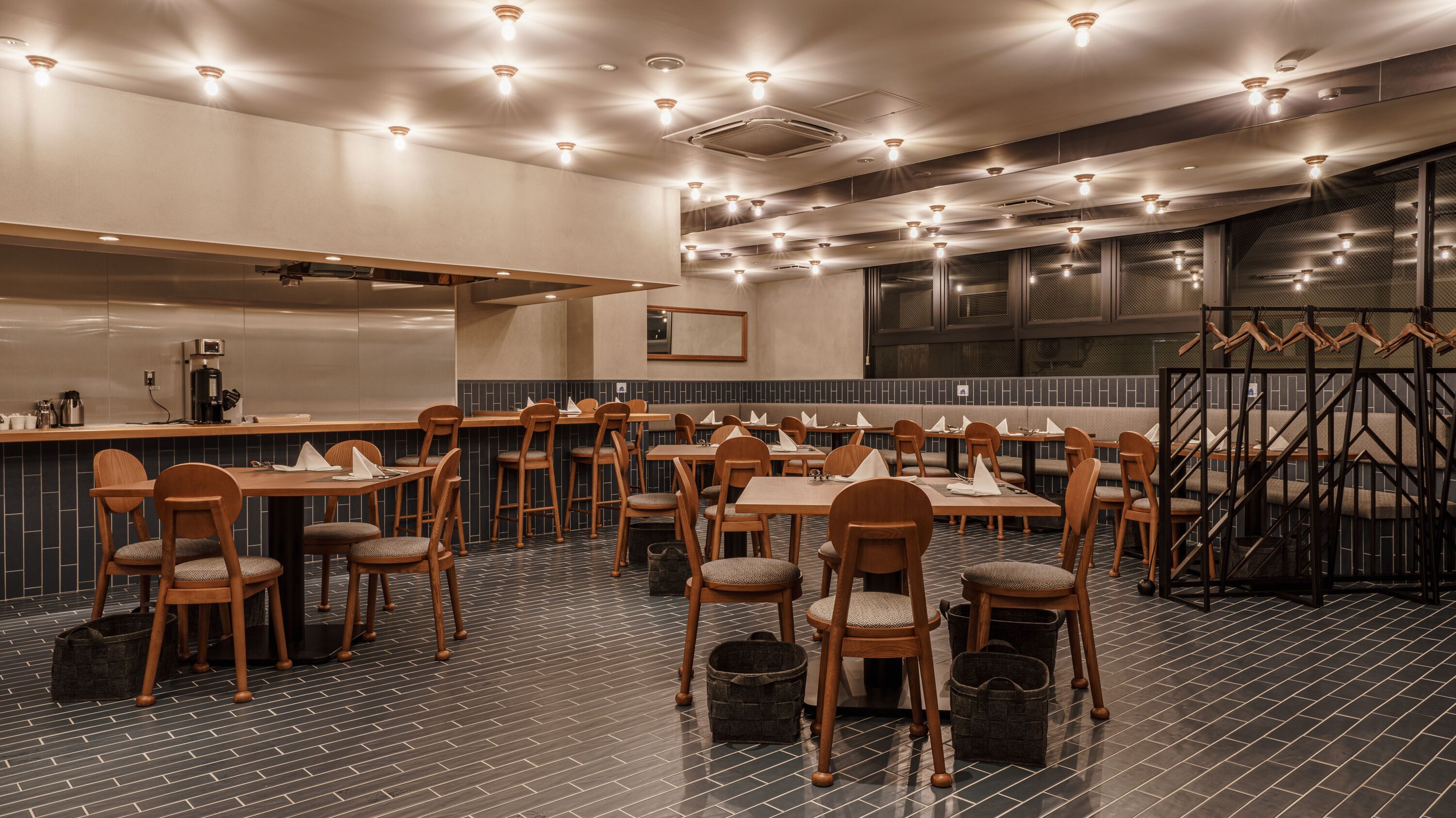 A restaurant with a modern interior, featuring wooden tables and chairs, a bar area, and a patterned floor.