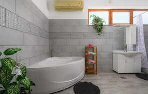 A modern bathroom with a freestanding bathtub, a wooden shelf with towels, a sink, and a window with a plant. - Amazing home in Smoljanci (Smoljanci)