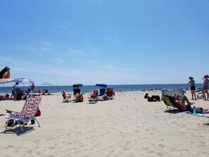 Une plage avec plusieurs chaises longues et des parasols, quelques personnes, et une vue dégagée sur l’océan.