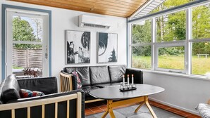 Una habitación acogedora con un sofá de cuero negro, una pequeña mesa redonda con velas y dos ventanas amplias que dan a vistas de vegetación.
