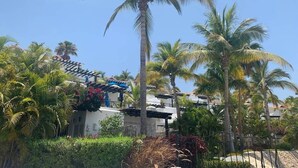 A resort with palm trees, a pool, and a building with a tiled roof. - Luxurious Condo with Ocean view near to San Jose (San José del Cabo)