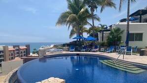 A pool with lounge chairs and umbrellas, palm trees, and a view of the ocean. - Luxurious Condo with Ocean view near to San Jose (San José del Cabo)