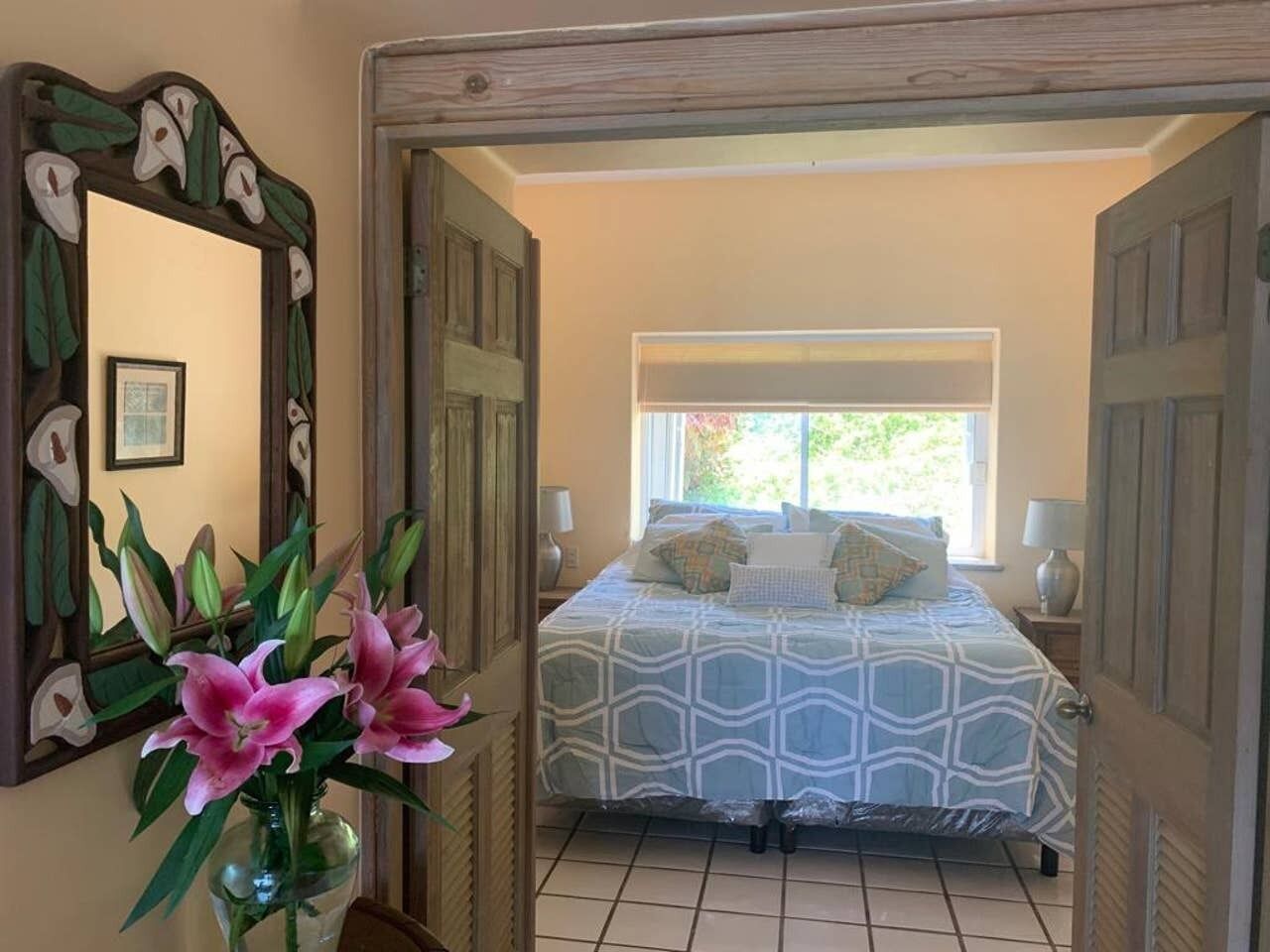 A bedroom with a bed, a nightstand, a lamp, and a window with a view of greenery.