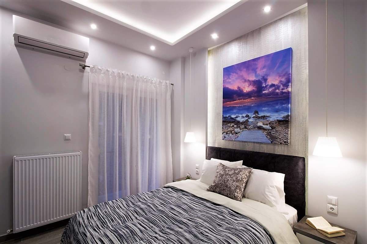 A modern hotel room with a bed, a painting, a radiator, and a window with curtains.