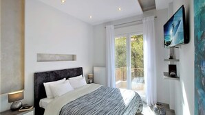 A modern bedroom with a large bed, a TV mounted on the wall, and a balcony with a view. - Thessaloniki Historic Center - Metro Apartment (Thessaloniki)