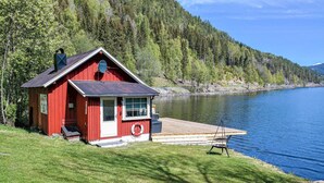 Una cabaña roja junto a un lago, con un muelle y una silla.