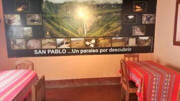 A room with two wooden tables, each covered with a red tablecloth. A large poster on the wall displays various photographs of San Pablo, including a waterfall and a mountain landscape.