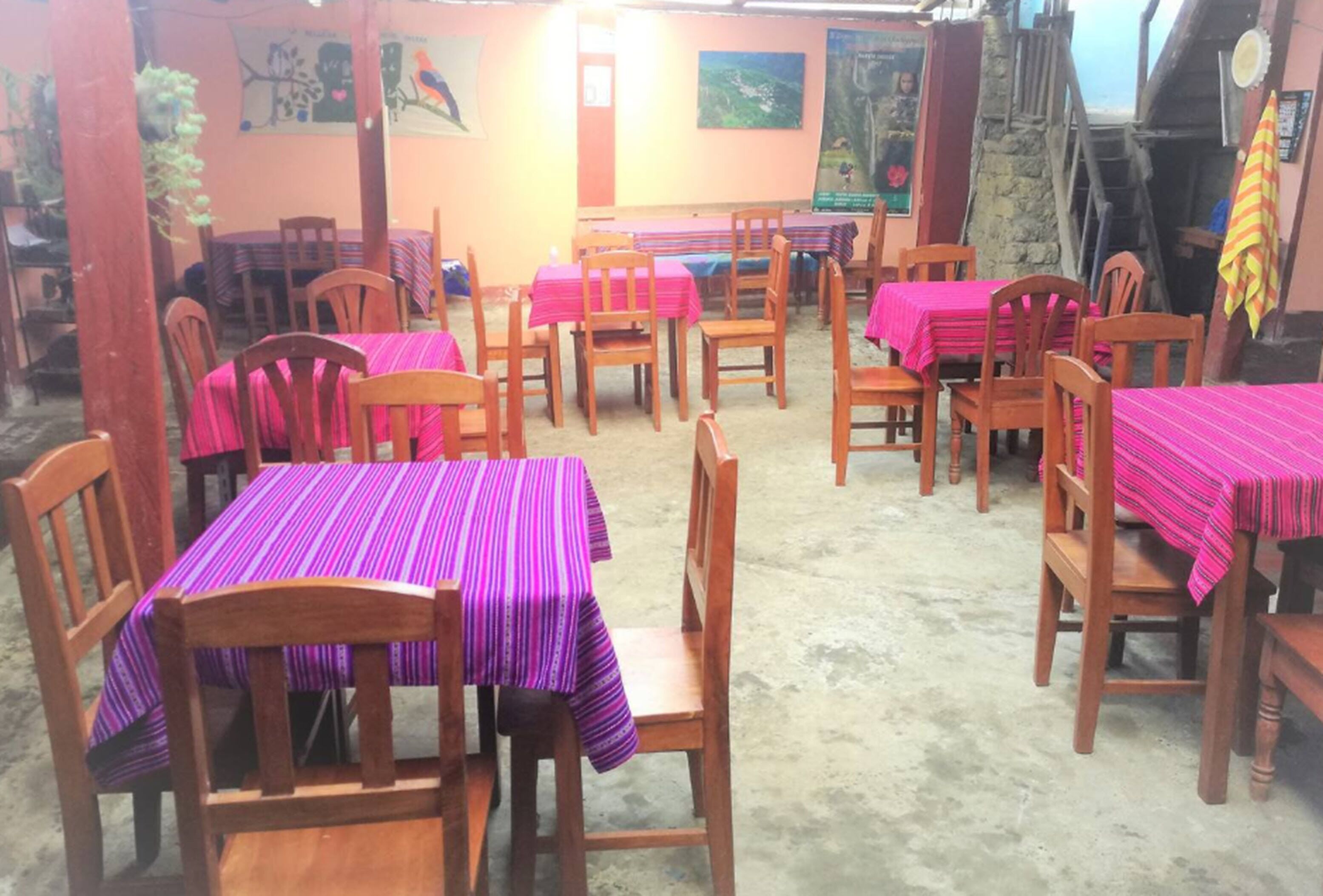 A restaurant with multiple tables covered with pink tablecloths and wooden chairs.