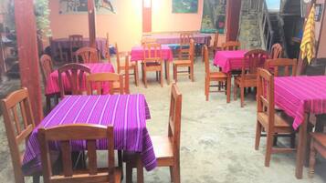 A restaurant with multiple tables covered with pink tablecloths and wooden chairs.