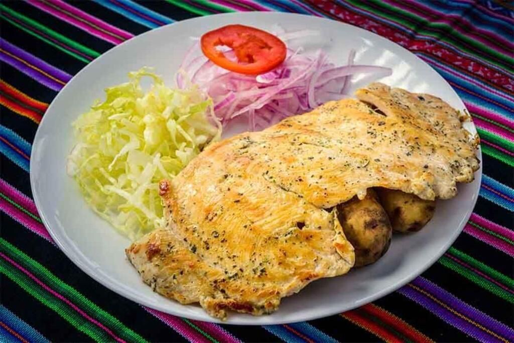 A plate with grilled chicken, boiled potatoes, shredded cabbage, and sliced red onions.