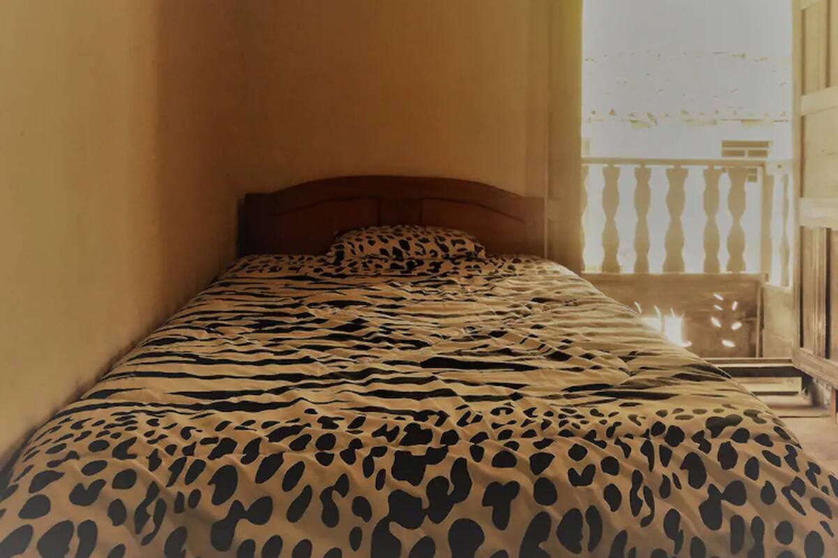 A small room with a bed featuring a leopard print bedspread, a wooden headboard, and a balcony with a railing.