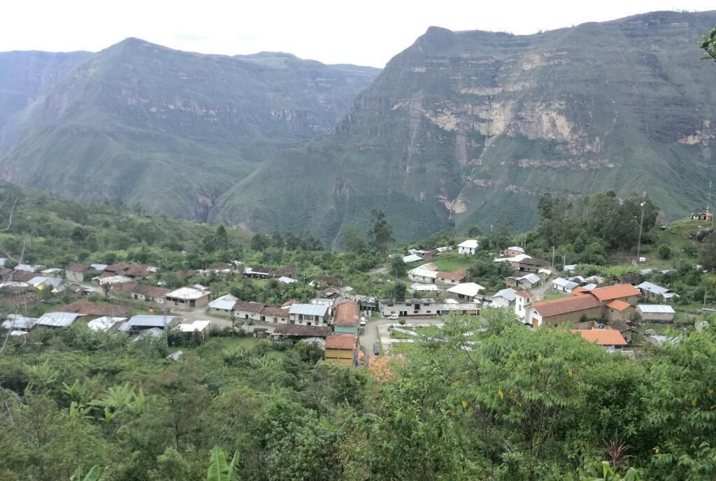 A village nestled in a valley with houses surrounded by lush greenery and mountains in the background.