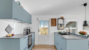 A modern kitchen with light blue cabinets, a central island, a coffee maker, and a view through the door. - Cozy home in Nysted with house sea view (Nysted)