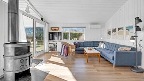 A spacious living room with a large blue sofa, a wooden coffee table, and a modern fireplace. - Cozy home in Nysted with house sea view (Nysted)