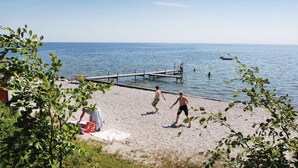 A beach with a wooden pier extending into the water, a sandy shore, and a few people swimming and walking. - Cozy home in Nysted with house sea view (Nysted)