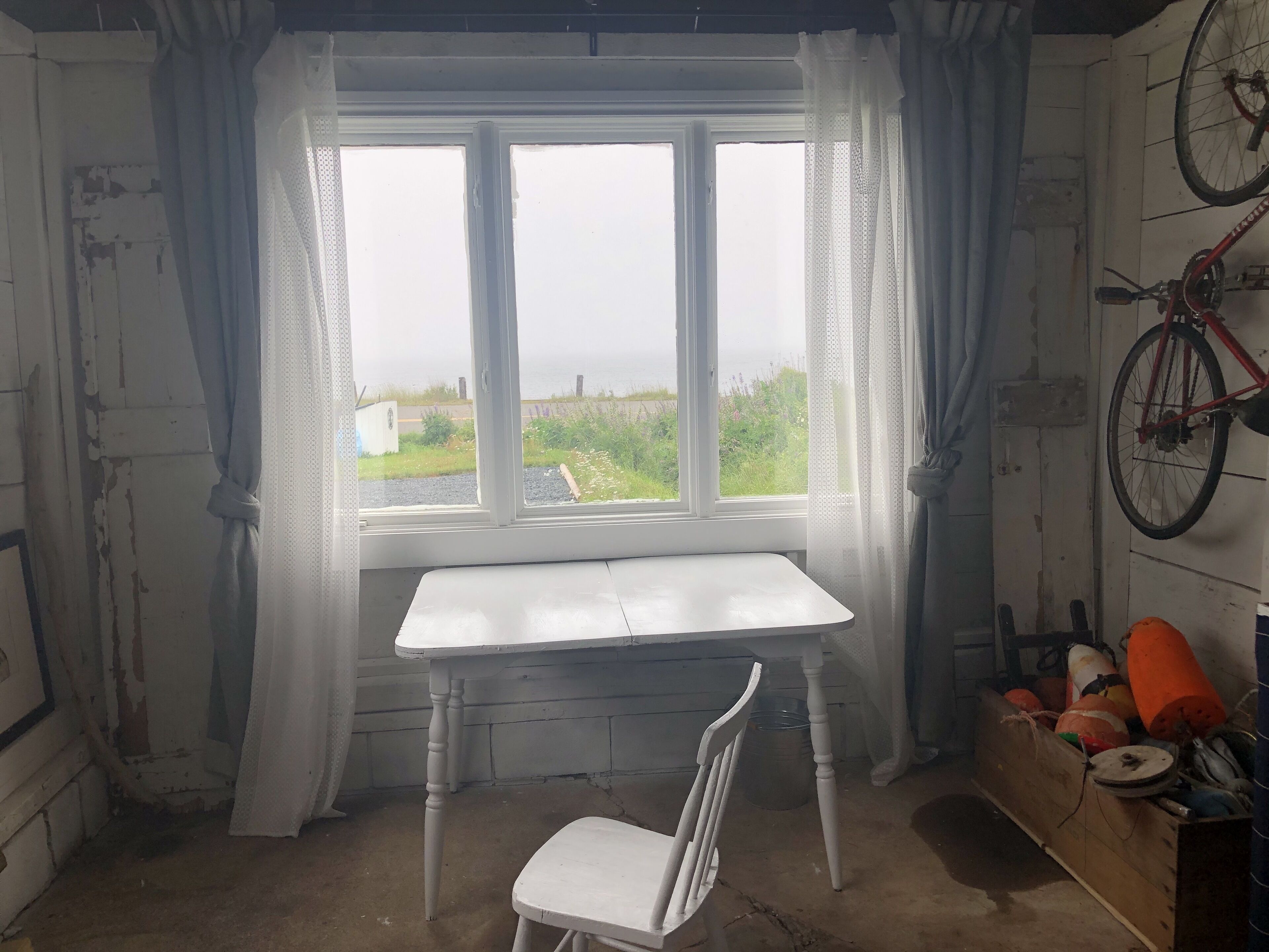 A room with a white table and a white chair, a bicycle, and a box of orange items.