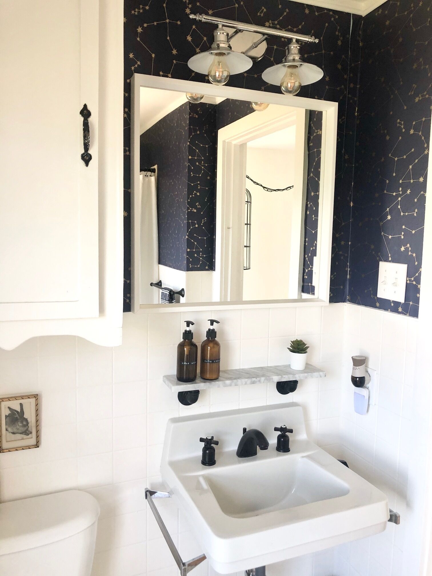 A bathroom with a white sink, black and white tiled walls, a mirror, and a ceiling light fixture.