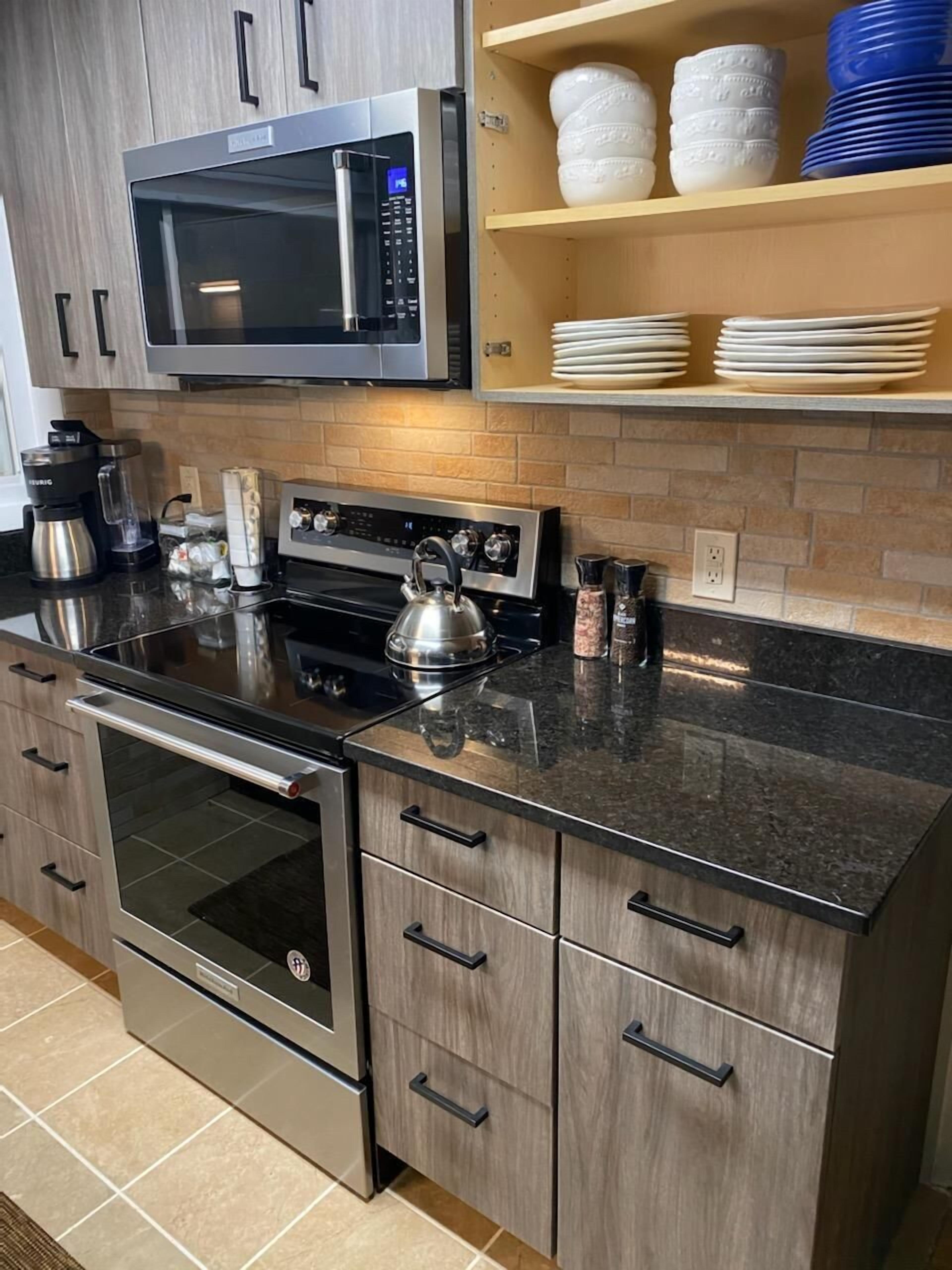 A kitchen with a stainless steel microwave, a kettle, a coffee maker, and a built-in oven.