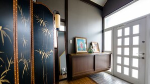 A hallway with a wooden floor, a dark wall with bamboo artwork, a cabinet with framed pictures, and a door with glass panels. - Cozy Vacation Stay Fuji Kawaguchiko (Fujikawaguchiko)