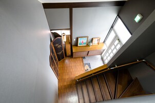 Una escalera de madera con barandilla, que conduce a una habitación con piso de madera, un escritorio con una silla y una ventana con luz natural.