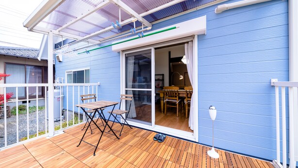 A blue building with a wooden deck, a sliding glass door, and a table with chairs. - Cozy Vacation Stay Fuji Kawaguchiko (Fujikawaguchiko)