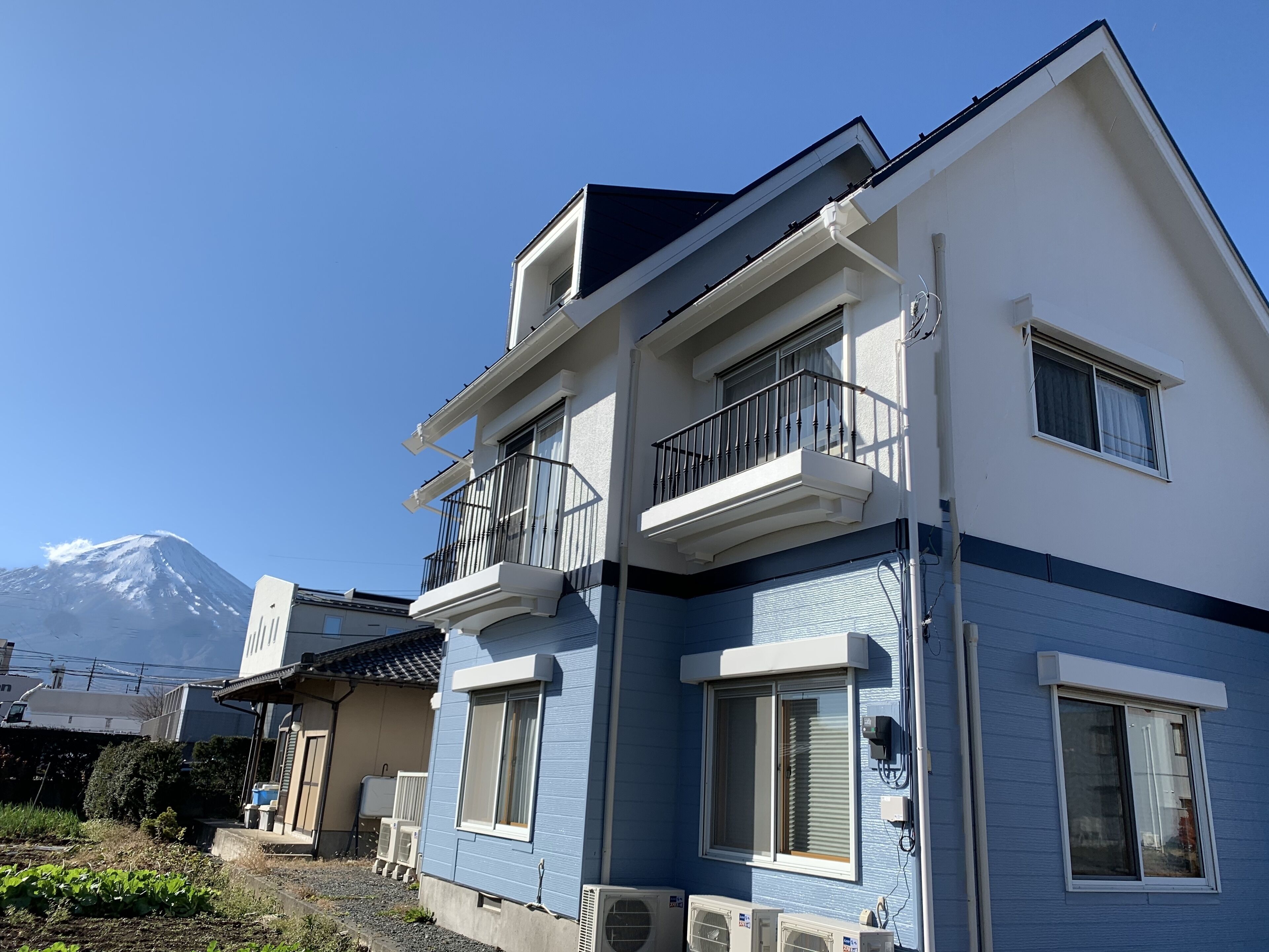 A two-story building with a balcony, a window with blinds, and an air conditioning unit.