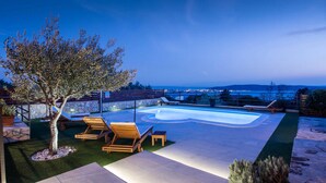 A swimming pool with a unique shape, surrounded by wooden loungers and a tree. - Amazing home in Kastel Sucurac (Kastel Sucurac)