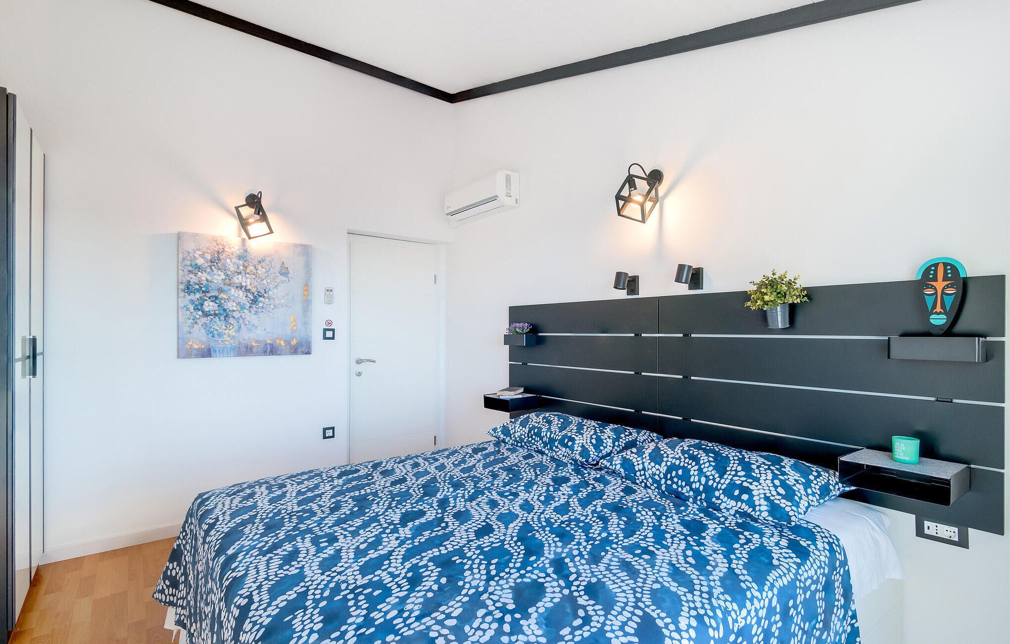 Ein modernes Schlafzimmer mit Bett, Nachttischen, einer Wandregal, einem Gemälde und einer Tür.