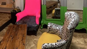 A room with a wooden floor, a pink chair, a patterned armchair, a green and white cabinet, and a potted plant. - Okinawa 13 (Naha)