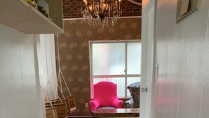 A hallway with a patterned wooden floor, a pink chair, a chandelier, and a window with a view. - Okinawa 13 (Naha)