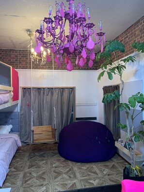 Ein Zimmer mit einem Etagenbett, einem violetten Sitzsack, einer Kristallleuchtre und einem Blumentopf.