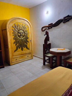 Ein Zimmer mit einem Bett, einem Nachttischchen mit Sonnendesign, einem Holzstuhl, einem kleinen Tisch und einer Wanddekoration.