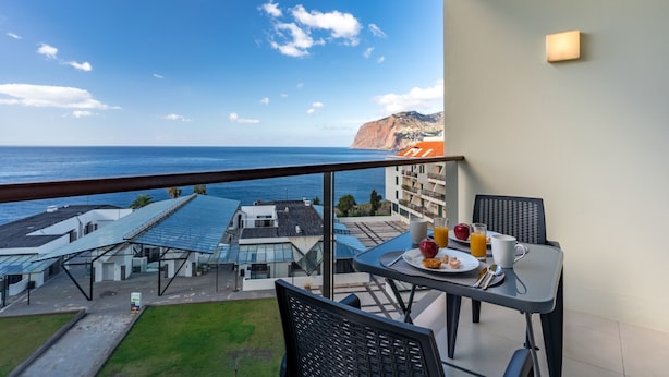 A balcony with a table set for breakfast, overlooking a coastal view with buildings and cliffs. - Centromar Bella Vista by Atlantic Holiday (Funchal)