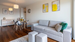 A modern living room with a grey sofa, ottomans, a dining area with a table and chairs, and a kitchen in the background. - Centromar Bella Vista by Atlantic Holiday (Funchal)