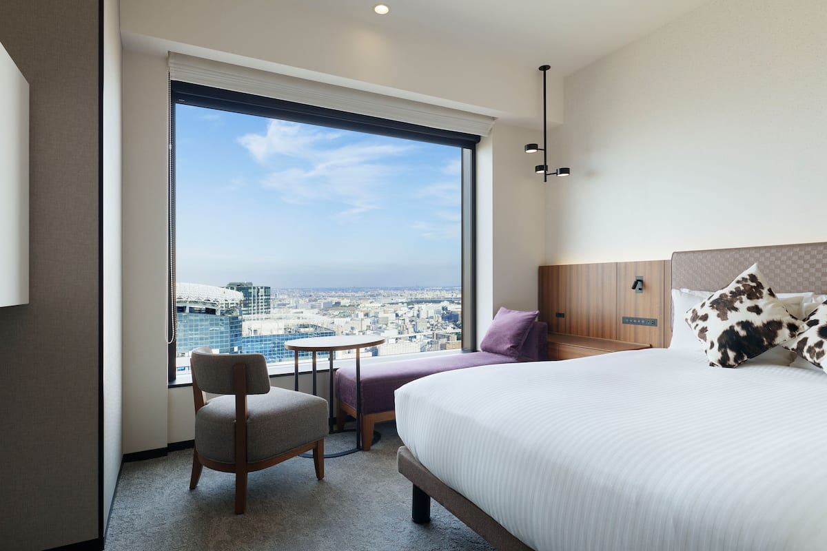 Habitación de hotel con una ventana grande, una cama, una silla y una mesita.