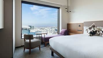 A hotel room with a large window, a bed, a chair, and a small table.