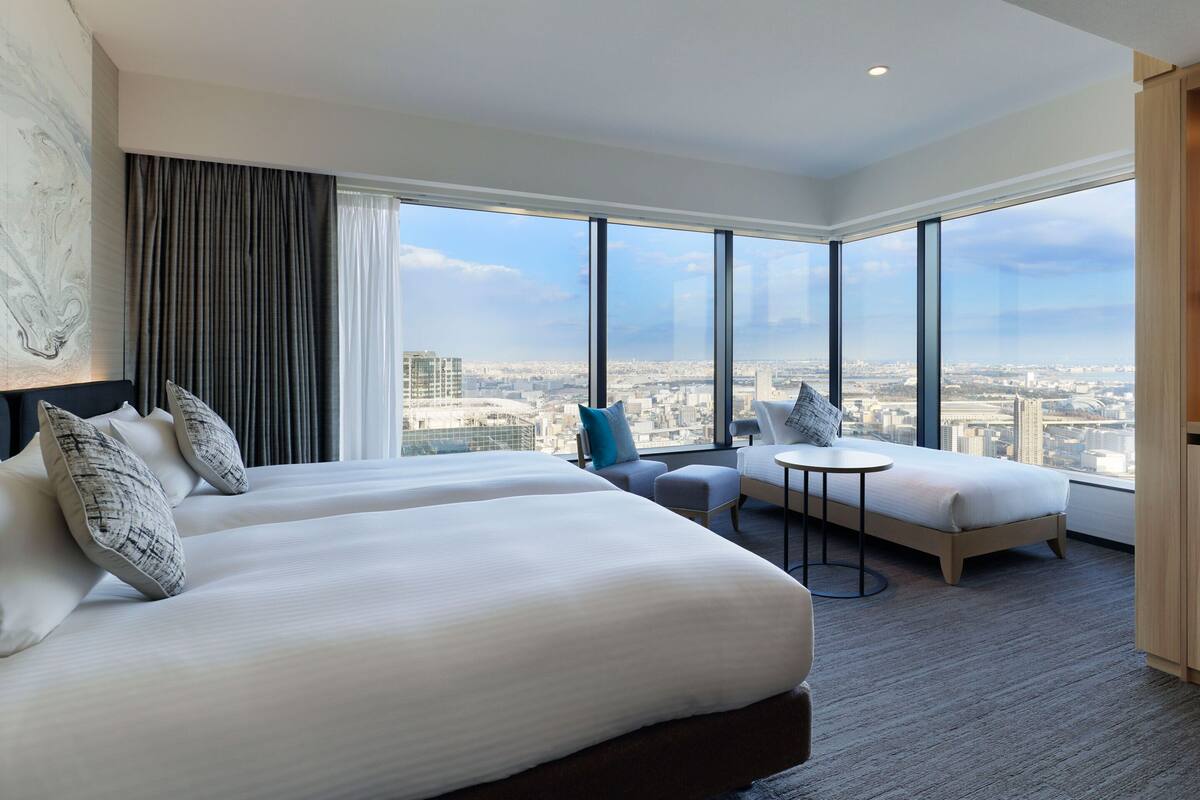 Habitación de hotel con una cama grande, un sofá, una mesita y vistas a la ciudad.