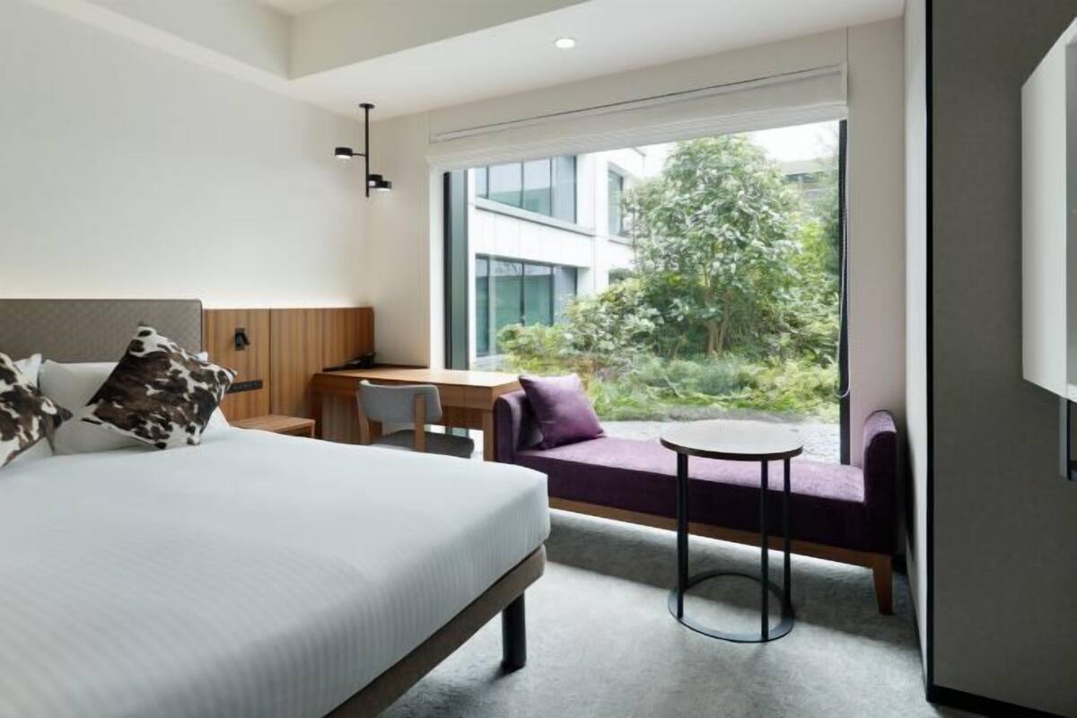 A modern hotel room with a bed, a desk, a chair, a small round table, and a sofa.