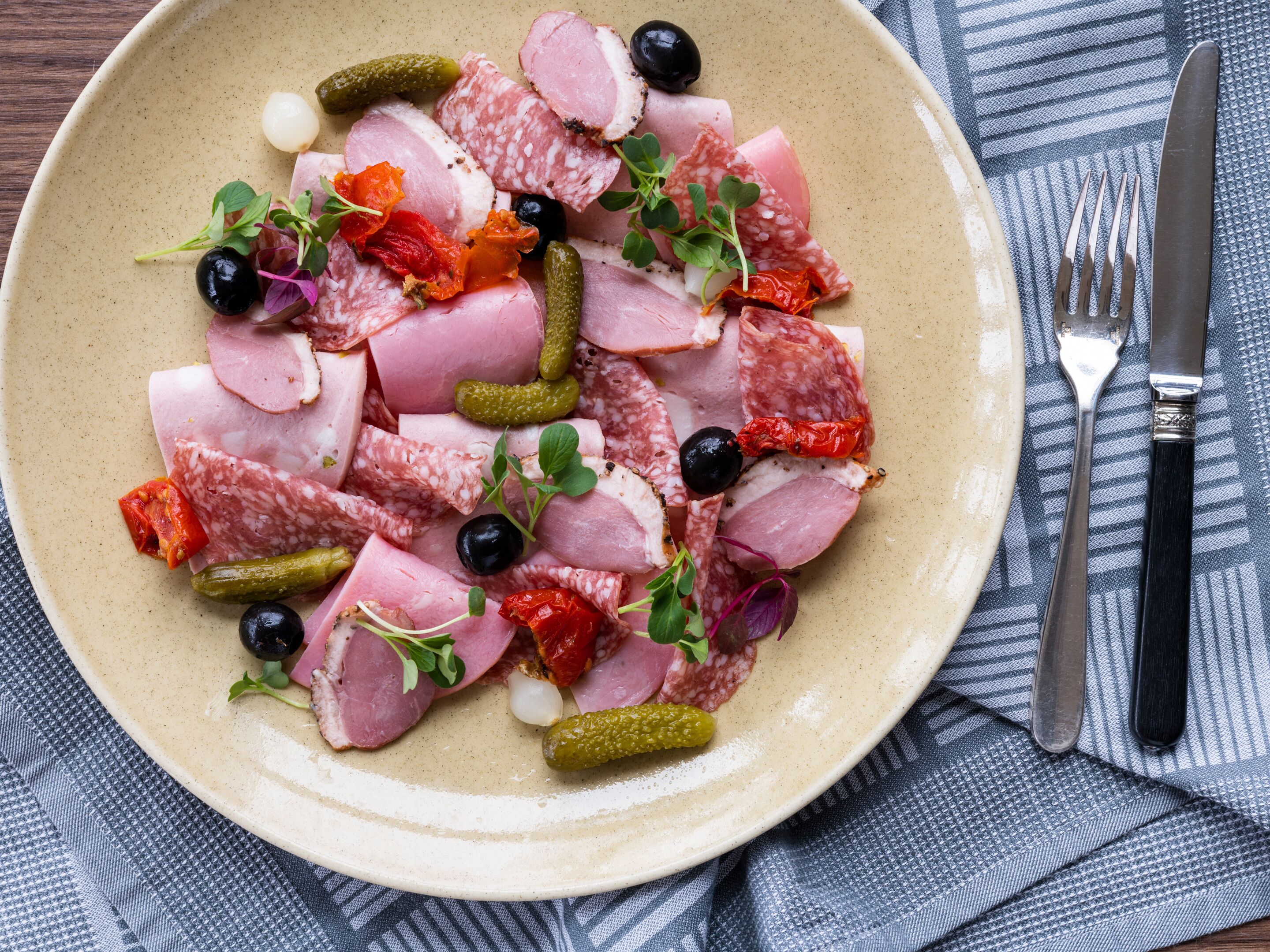 A plate of assorted meats and pickles on a beige plate.