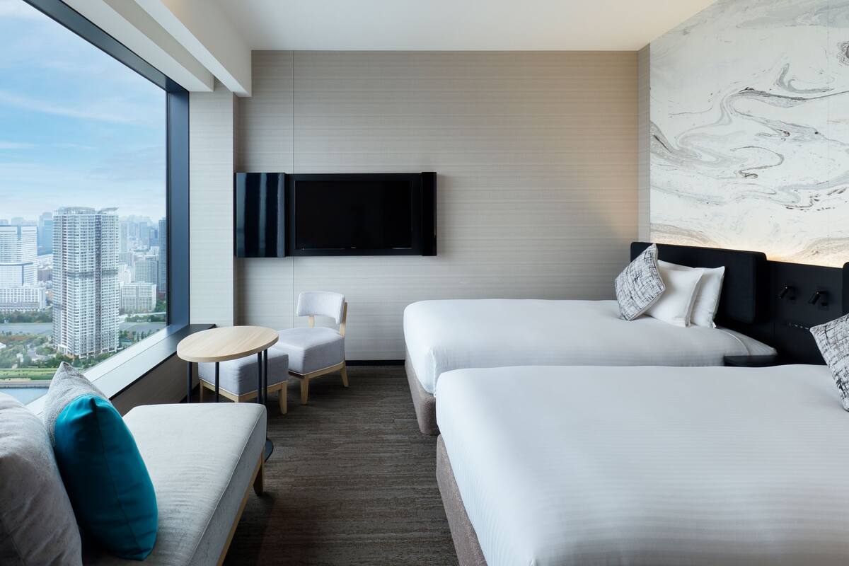 Habitación de hotel con dos camas, televisión, silla y vistas a la ciudad.
