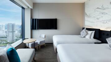 A hotel room with two beds, a TV, a chair, and a view of the city.