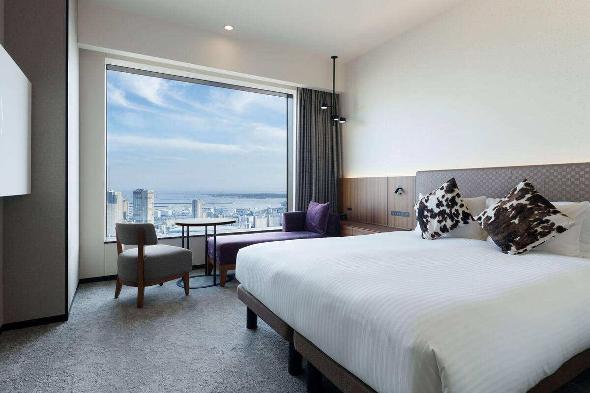 Una habitación de hotel con un ventanal grande, una cama, una silla y una mesita.