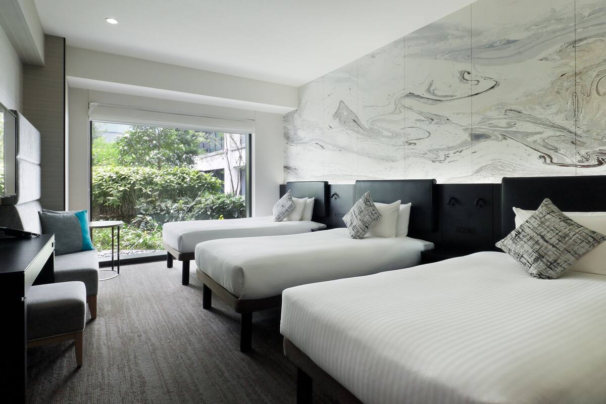 Habitación de hotel con dos camas, un escritorio y un ventanal con vistas a zonas verdes.