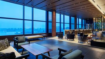 A spacious lounge area with large windows offering a city view, a bar area with seating, and a mix of modern and classic furniture.