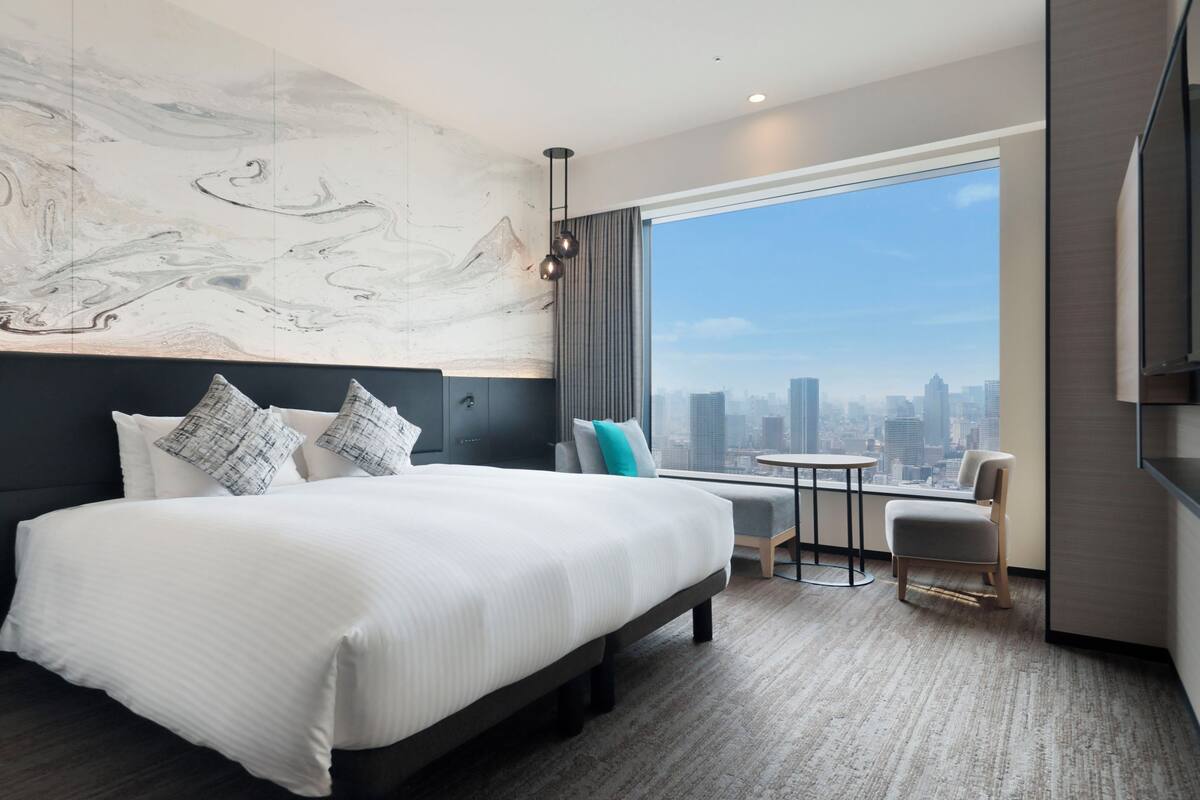 Una habitación de hotel moderna con una cama grande, una mesita, una silla y vistas a la ciudad.