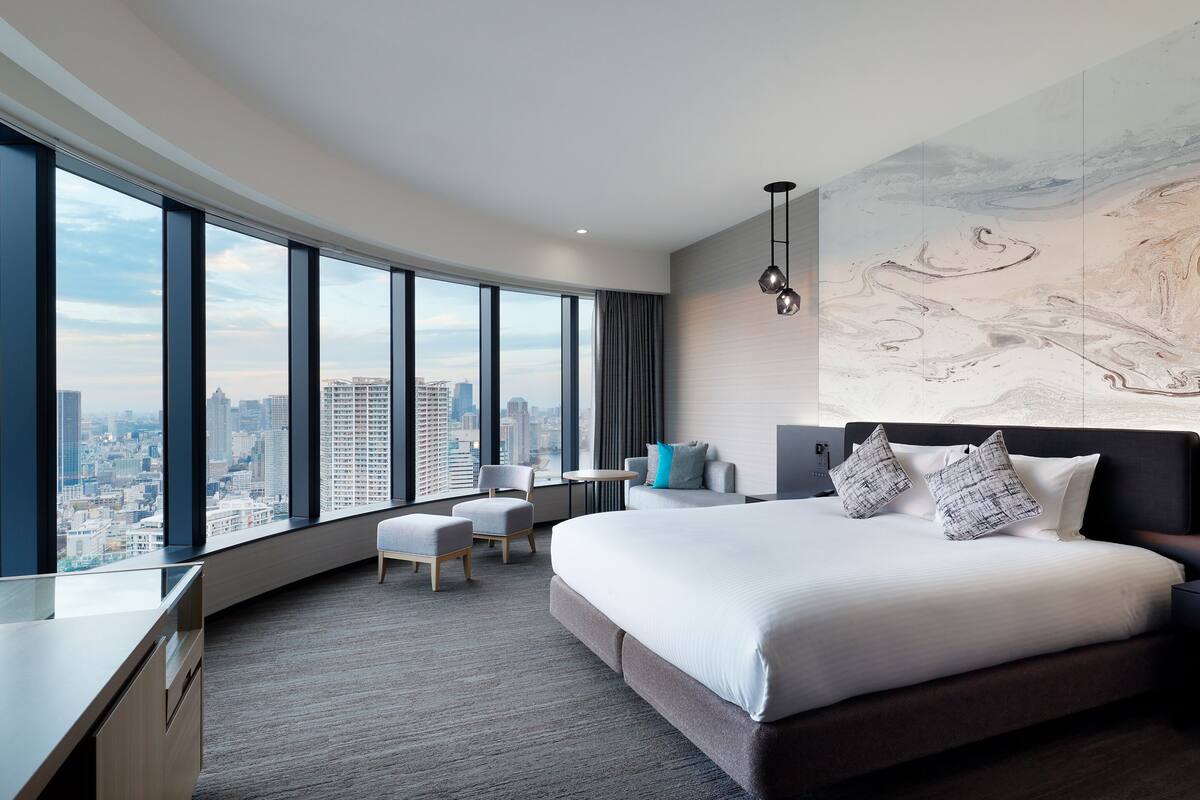 Una habitación de hotel moderna con una cama grande, un escritorio, una silla y vistas a la ciudad.